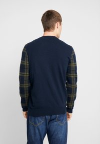 Pull marin avec des manches à carreaux vert et noir, col rond et poignets côtelés. Mélange de laine, coupe décontractée.