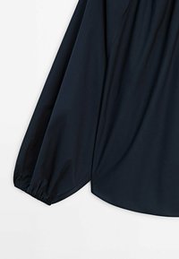 Manche longue noire de blouse avec poignet élastique sur un fond clair uni, montrant la texture du tissu et la forme du vêtement.