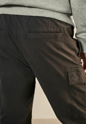 Pantaloni cargo neri con una texture liscia, dotati di tasche laterali e posteriori. Progettati con una vita elastica per il massimo comfort.