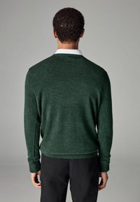 Jersey de color verde oscuro con cuello redondeado, puños acanalados y un ajuste ligeramente holgado. Tejido texturizado con un aspecto suave.