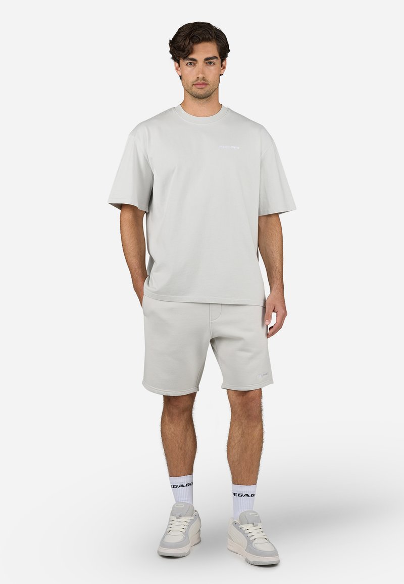 Hellgraues Baumwoll-T-Shirt mit kurzen Ärmeln und passenden Shorts, mit lockerer Passform und minimaler Markenkennzeichnung. Getragen mit hellen Sneakers.