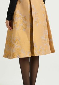Une jupe jaune longueur genou avec une broderie florale en tons or et argent, présentant un tissu subtilement texturé et une silhouette trapèze.