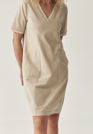 Beiges kurzes Kleid mit kurzen Ärmeln und V-Ausschnitt, zwei Fronttaschen, strukturiertem Stoff und kontrastierendem Abschluss entlang des Ausschnitts und der Ärmel.