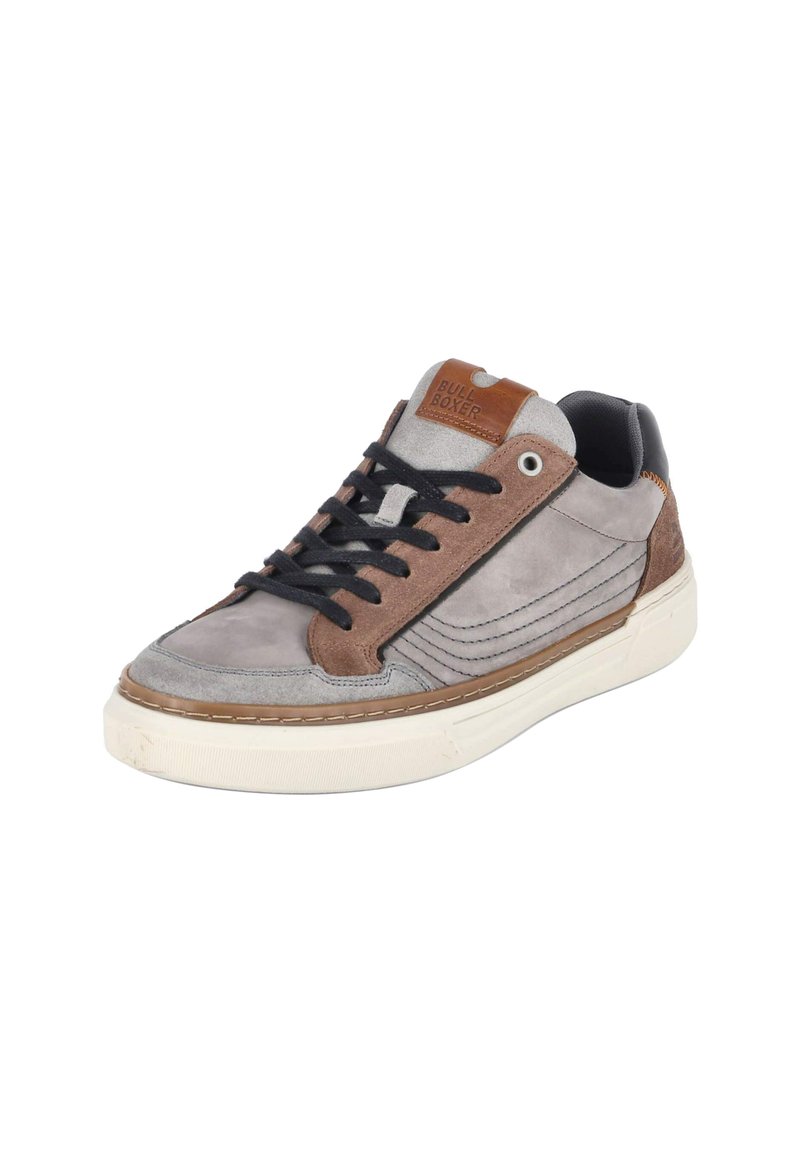 Grijze en bruine sneaker van suede en leer, met zwarte veters, een witte rubberen zool en een bruine logo-tag op de tong.