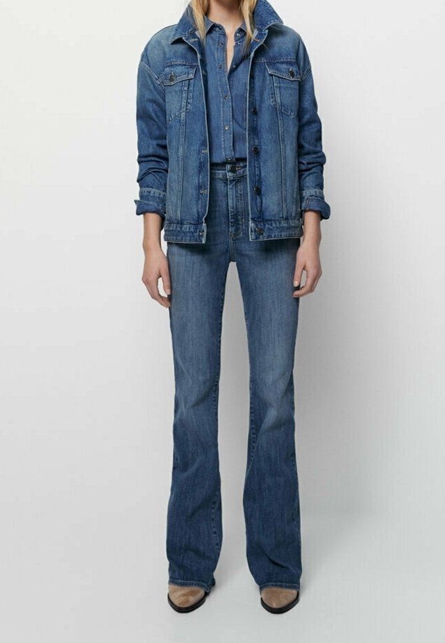 Denim-takki ja leveälahkeiset farkut keskitummassa sinisessä värissä; takissa on kaksi rintataskua, napitus ja kaulus; farkut istuvat tiukasti vyötäröllä.