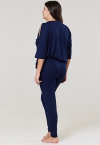 Námornícky modrý loungewear set, ktorý obsahuje voľný top s výrezmi na ramenách a úzke nohavice. Mäkkaná látka s hladkým povrchom.