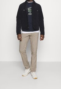 Námořnicky modrá manšestrová bunda přes modrou mikinu s potiskem, doplněná béžovými kostkovan�ými kalhotami a bílými teniskami.