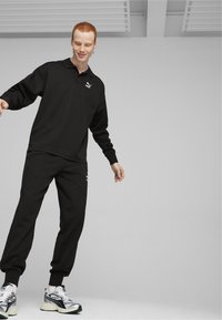 Musthave musta sportlik komplekt, millel on pikakäedega polo särk ja dressipüksid, mis sisaldavad diskreetset logo. Tekstureeritud kangas, mugav lõige ja soonikvarrukad.