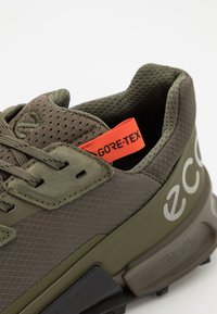 Olivgrön sneaker med Gore-Tex-märke, med texturerad mesh och släta läderdetaljer, stadig svart sula och framträdande logotypdetalj.