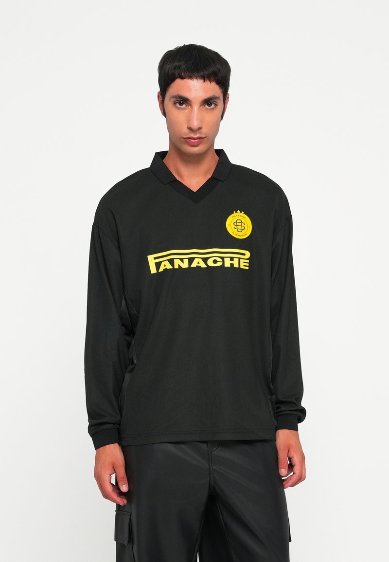 Schwarzes Langarmshirt mit V-Ausschnitt, das eine auffällige gelbe Grafik mit der Aufschrift "PANACHE" und einem runden Logo auf der Brust zeigt.