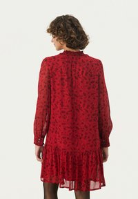 Rotes Blumenkleid mit langen Ärmeln, gerafftem Ausschnitt und gestuftem Saum. Leichter Stoff mit transparenter Textur und geknöpften Manschetten.