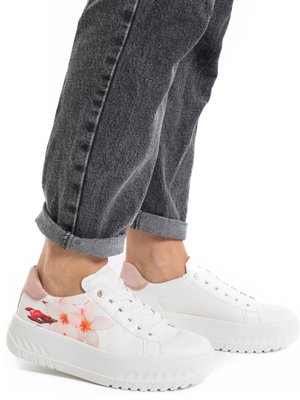 Hvide platformsneakers med pink blomsterdesign på siderne, båret med op rullede mørkegrå jeans, vist fra siden og bagfra.