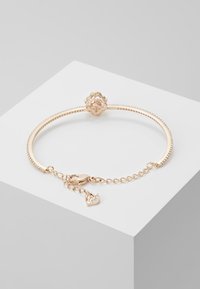 Bracciale in oro rosa con una fascia texturizzata, chiusura decorativa con design a fiore e un piccolo charm a forma di cigno con accenti brillanti.