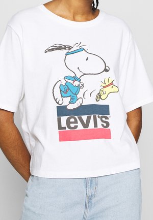 Osoba nosząca białą koszulkę Levi's z postaciami Snoopy i Woodstock w niebieskim stroju sportowym biegnące z przodu.