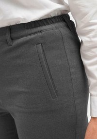 Grijze broek met een elastische tailleband, voorzien van een zijzak en een gladde, textuurstof. G gecombineerd met een wit shirt.