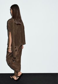 Completino in top e pantaloni marroni a pieghe con vestibilità ampia. Tessuto morbido e texturizzato con un design drappeggiato. Top aperto sui lati e sandali piatti.
