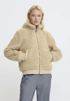 Beige Kunstfelljacke mit hohem Kragen, Reißverschluss vorne und elastischen Bündchen. Verfügt über eine strukturierte Oberfläche und einen gerippten Saum für zusätzliche Details.