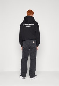 Black hoodie with white text “DROWNED ANGELS @PEQUS” on the back. Paired with loose black cargo pants and white sneakers.
