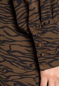 Brun tigerrandig långärmad blus med en samlad manschett med tre runda knappar och en slät tygstruktur.