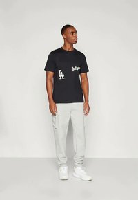 Černé tričko s bílými nápisy "Los Angeles" a "LA", kombinované se světle šedými cargo kalhotami a bílými teniskami. Jednoduchý a ležérní design.