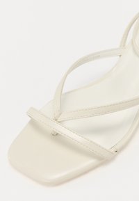 Beige sandaalit, joissa on neliön muotoinen kärki, valmistettu sileästä nahasta. Ominaisuuksina ohuet, ristikkäiset hihnat, jotka luovat minimalistista tyyliä.