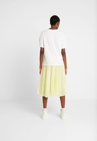 Camiseta blanca de manga corta combinada con una falda amarilla clara, con pliegues, hasta la rodilla, y zapatillas blancas. Diseño minimalista y ligero.