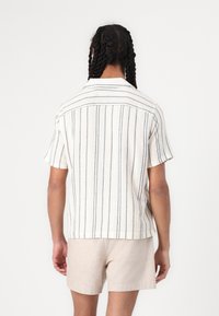 Korte mouwen shirt in crème met marineblauwe strepen, gestructureerde stof en een kraag. Draag het met beige shorts, bekeken vanuit de achterkant.