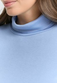 Close-up van een vrouw die een lichtblauwe geribde coltrui draagt, waarbij haar ondergezicht en nek in beeld zijn.