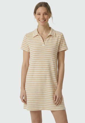 Frau lächelt und trägt ein kurzärmliges, kragenbesetztes Kleid mit beige- und orangefarbenen horizontalen Streifen vor einem einfarbigen hellen Hintergrund.