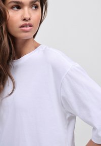 T-shirt bianco in cotone con vestibilità rilassata, scollo rotondo e cuciture delle spalle scese, caratterizzato da una texture liscia.