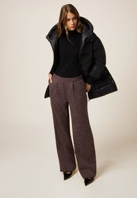 Czarna kurtka puchowa, czarny dzianinowy top oraz brązowe, teksturowane spodnie o szerokich nogawkach z bocznymi kieszeniami. Całość dopełniają czarne, szpiczaste buty.