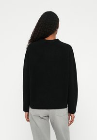 Svart strikket genser med rund hals, avslappet passform og lange ermer. Strukturert stoff; kombinert med lysegrå jeans.