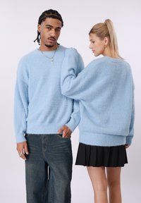 Svetlomodro puhasto pleten pulover z ohlapnim krojem, rebrastimi manšetami in spodnjim robom, kombiniran s temnimi jeansa hlačami in črno plisirano krilo.