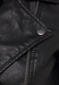 Giacca in pelle nera con superficie testurizzata, cerniera asimmetrica e dettaglio con bottone a pressione sul colletto, caratterizzata da un design diagonale.