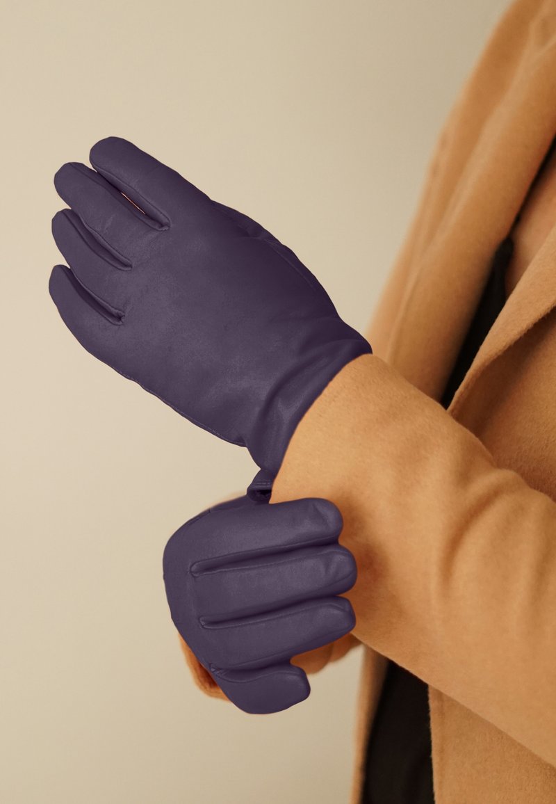 Purple leather gloves with a smooth texture, featuring a fitted design and soft lining, held against a beige coat.