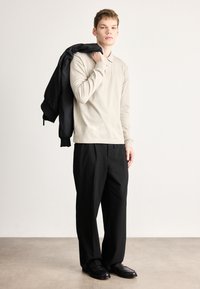 Bež dolgo rokav polo majica z ovratnikom, nošena s črnimi širokimi hlačami in črnimi čevlji; črna jakna premetena čez roko.