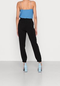 Niebieska ribbed kamizelka, czarne tapered jogger pants oraz jasnoniebieskie sandały na słupku, widok z tyłu na neutralnym tle.