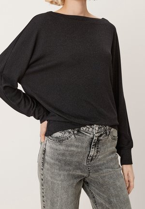 Schwarzes Langarmoberteil mit lockerer Passform, breitem Halsausschnitt und leichtem Glitzer. Kombiniert mit hochtaillierten, ausgeblichenen grauen Jeans.