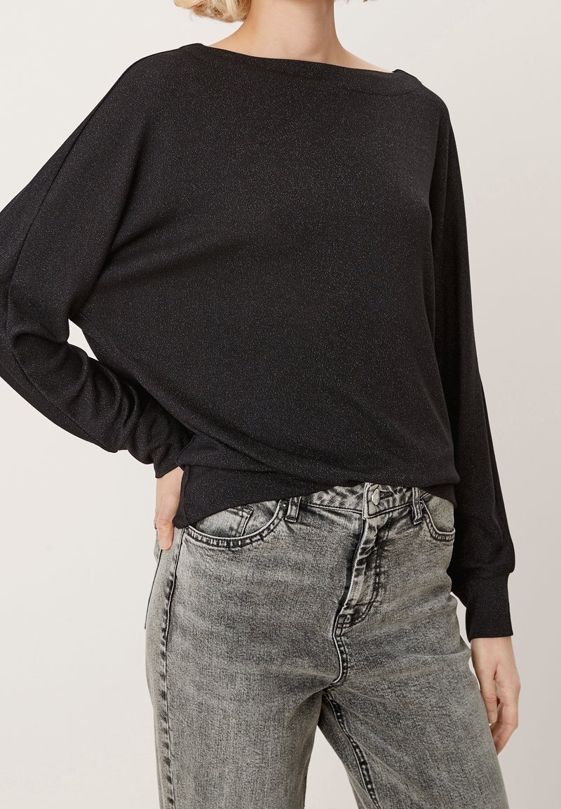 Svart långärmad topp med lös passform, med en vid halsringning och lätt glans. Matchad med hög midja, blekta grå jeans.