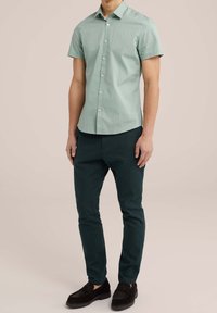 Ljusgrön kortärmad skjorta med knapplist, bärs med mörkgröna slim-fit byxor och svarta loafers. Snygg tygets struktur.