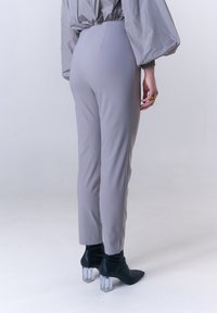 Graue, eng anliegende Hose mit glatter Textur und schmal zulaufender Form, kombiniert mit schwarzen Stiefeletten mit transparenten Blockabsätzen.