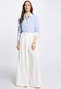 Camicia a righe blu chiaro con colletto bianco, abbinata a pantaloni bianchi a gamba larga con sottili dettagli in metallo.