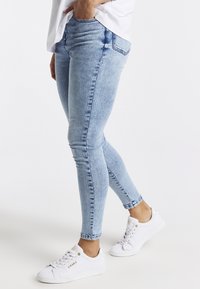 Jeans skinny de denim azul claro con una textura descolorida, con bolsillos laterales y un ligero efecto de desvanecimiento, combinados con zapatillas blancas.