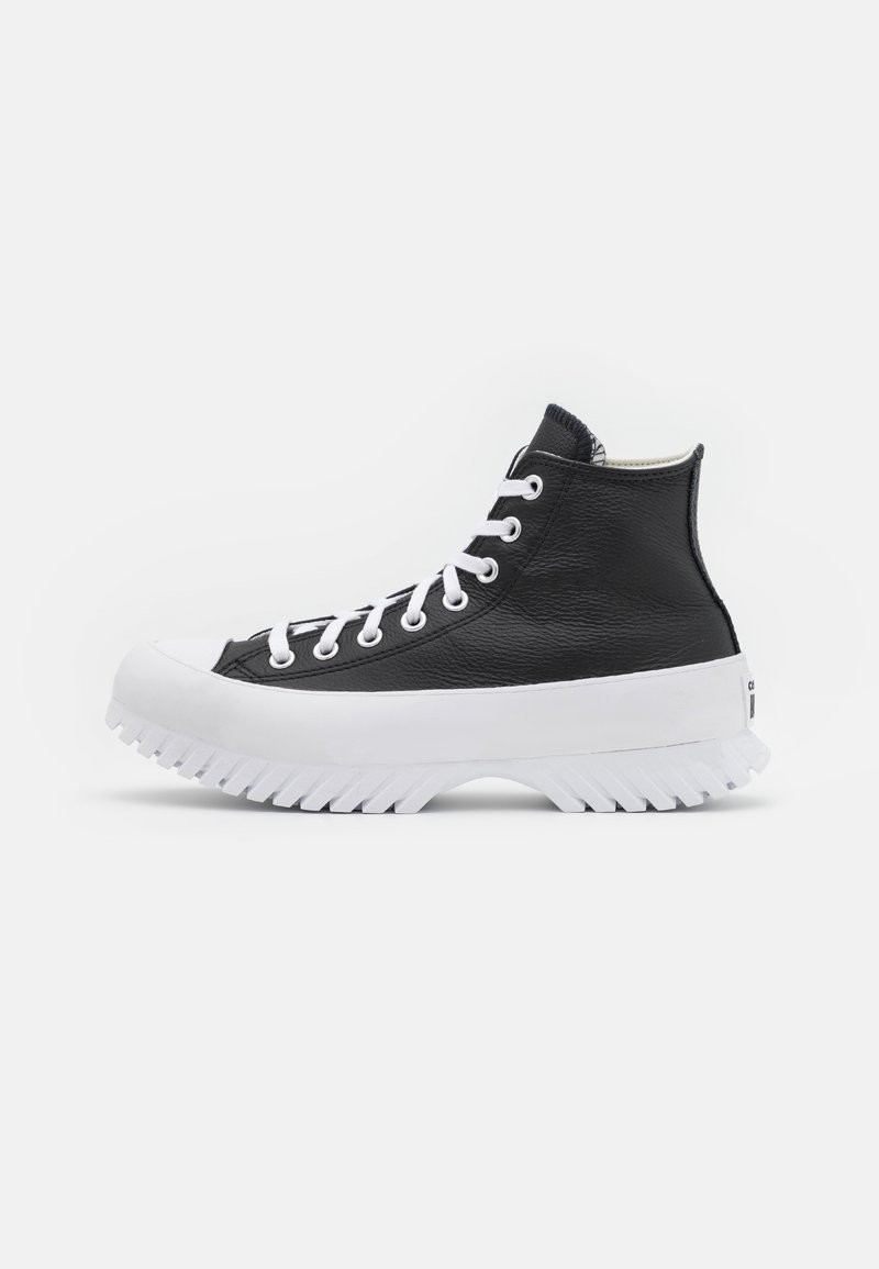 Baskets montantes noires avec lacets blancs et semelle épaisse blanche rainurée, vues de profil sur un fond gris clair.