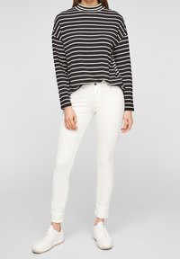 Musta-valkoiset raidalliset pitkähihainen paita yhdistettynä valkoisiin slim fit -farkkuihin ja valkoisiin tossuihin, joissa on rento ja mukava siluetti.