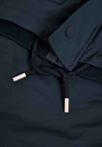 Chaqueta con capucha azul oscuro que presenta una cinturilla de punto, textura de nailon, cordón con puntas de bronce y detalles de botones a presión negros.