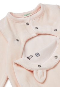 Mono de peluche rosa con botones a presión. Presenta un exterior suave, un forro interior con bordado y acentos de orejas en la capucha. Textura suave.