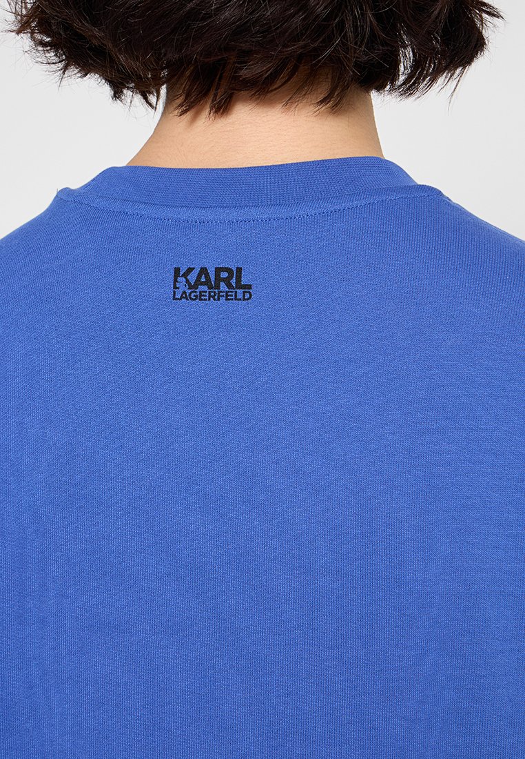 Camiseta de algodón azul con cuello redondo acanalado y el logo impreso en negro "KARL LAGERFELD" en la parte posterior, cerca del cuello.