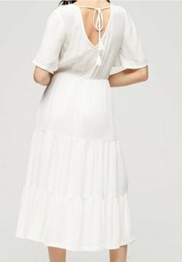 Biała, warstwowa sukienka z krótkimi rękawami, teksturowana, z dekoltem w kształcie litery V z tyłu oraz zawiązywaniem z frędzlami. Lekka i zwiewna konstrukcja.