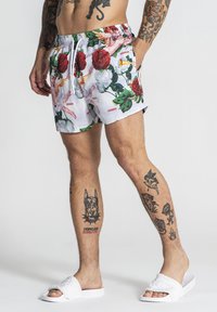 Shorts de bain fleuris avec une base blanche, ornés de roses rouges et de feuilles vertes. Taille élastique et cordon de serrage pour un ajustement optimal.